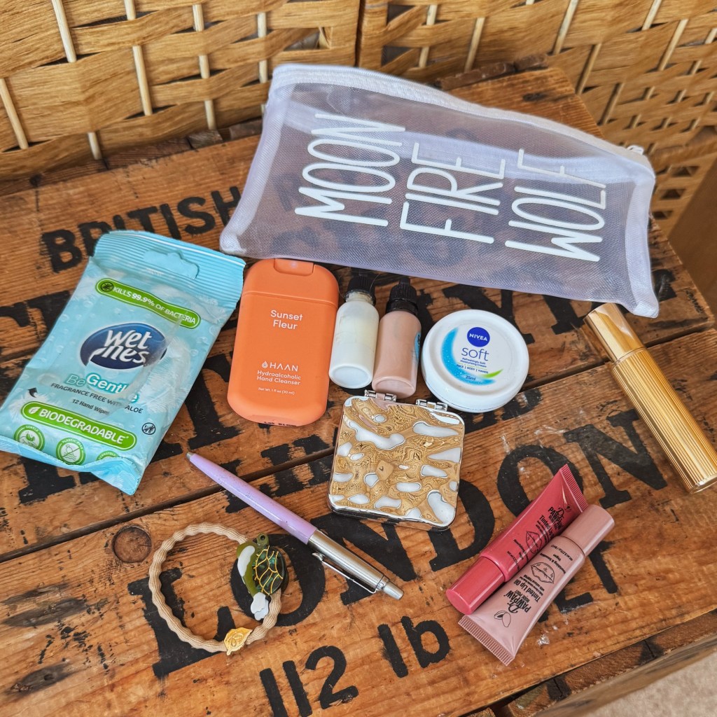     Contents of a small personal-care pouch, including hand sanitiser, moisturiser, lip balm, perfume, wet wipes and a hair tie.